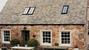 Un bâtiment en pierre avec deux fenêtres, une porte et un banc à l’extérieur.