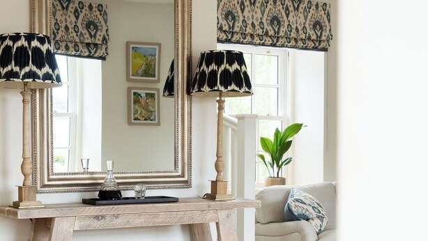Una habitación con un espejo grande, dos lámparas, una consola, un sofá y una ventana con cortina decorada.