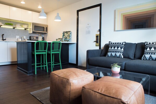 Eine moderne Küche mit Mikrowelle, grünen Stühlen und einem Essbereich. Es gibt ein Sofa mit gemusterten Kissen und einen Couchtisch mit einer Pflanze.