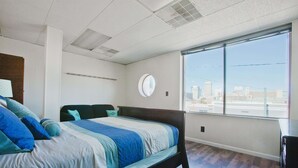 Ein modernes Schlafzimmer mit einem großen Bett, einem runden Spiegel und Blick auf die Stadt durch ein großes Fenster.
