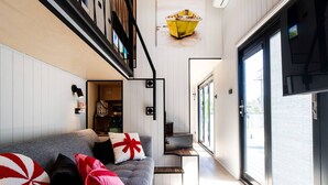 Een moderne woonkamer met een grijze bank, een klein tafeltje en een trap die naar een verdieping leidt.