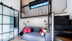Een moderne woonkamer met een grijze bank, een houten trap en een schuifdeur van glas.