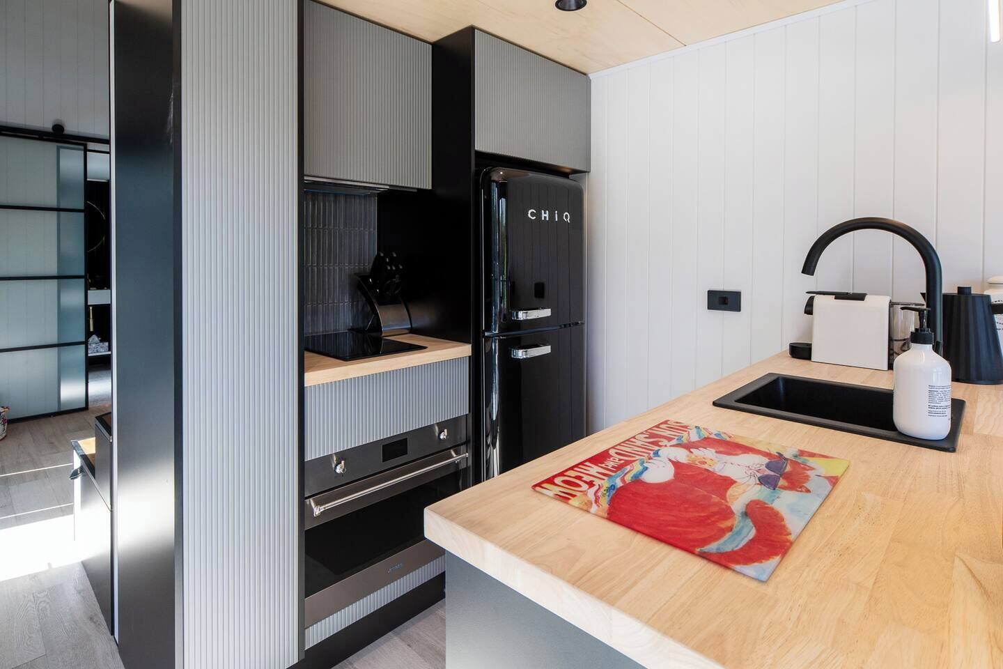 Una cucina moderna con frigorifero nero, piano di lavoro in legno e lavello.