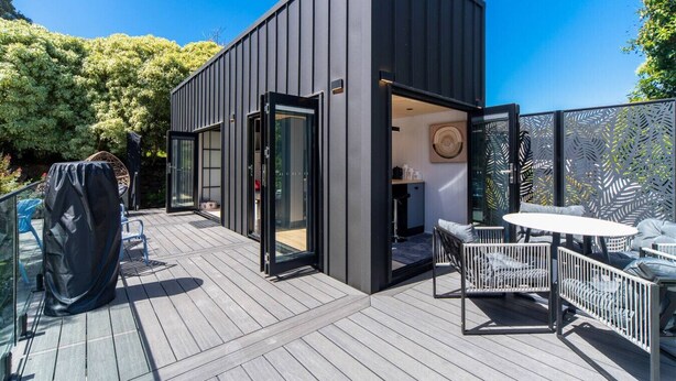 Een modern terras buiten met een houten vloer, een overdekte zithoek en een glazen deur naar een binnenruimte.