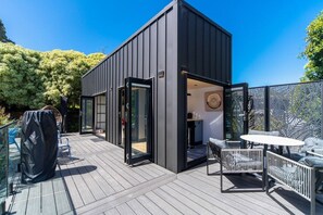 Een modern terras buiten met een houten vloer, een overdekte zithoek en een glazen deur naar een binnenruimte.