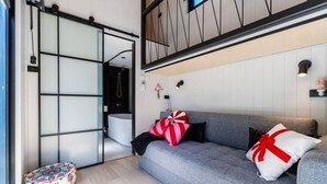 Een moderne woonkamer met een grijze bank, een klein rond tapijt en decoratieve kussens.