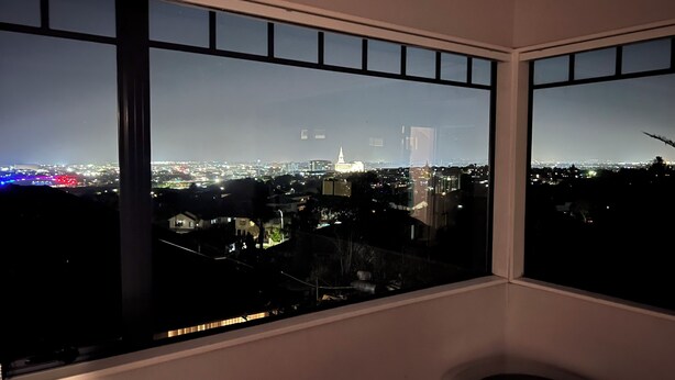 A room with large windows offering a nighttime cityscape view, including a prominent building with a spire. - Private Family Home With Four Bedrooms (Manukau)
