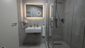 A modern bathroom with a glass shower enclosure, a built-in sink with a mirror, and a towel rack. - HarmoNest Rheydt Apartments 301 (Mönchengladbach)