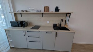 A modern kitchen with a wooden countertop, a built-in sink, and a microwave. There are cabinets with drawers and a shelf above the countertop holding glasses and a cutting board. - HarmoNest Rheydt Apartments 301 (Mönchengladbach)