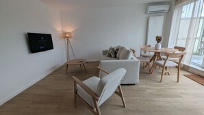 A modern living room with a sofa, a round table, and chairs. There is a floor lamp and a flat-screen TV mounted on the wall. - HarmoNest Rheydt Apartments 301 (Mönchengladbach)