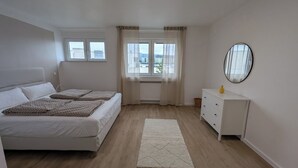 A bedroom with a bed, a dresser, a mirror, and a window with curtains. - HarmoNest Rheydt Apartments 301 (Mönchengladbach)