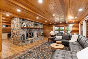 L’intérieur d’une cabane en rondins, avec une cheminée en pierre, un canapé en cuir et un tapis à motifs.