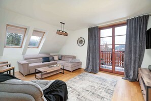 Ein modernes Wohnzimmer mit einer Eckcouch, einem Couchtisch, einem Teppich und einem großen Fenster mit Vorhängen.