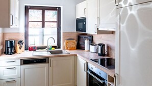 Een moderne keuken met een vaatwasser, fornuis, magnetron en een raam met jaloezieën.