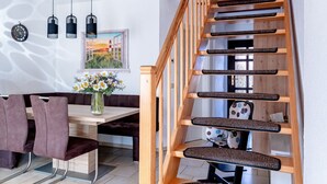 Een modern interieur met een houten trap, een eetgedeelte met een houten tafel en stoelen, en een schilderij aan de muur.