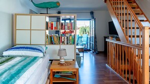 Een slaapkamer met een bed, een boekenkast, een bureau met een lamp en een trap.