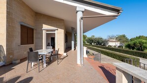 A covered patio with a table and chairs, a stone wall, and a view of a garden. - Villa 'Tubola' with Shared Pool, Wi-Fi and Air Conditioning (Lizzanello)