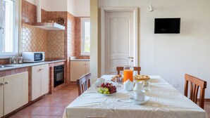 A kitchen with a microwave, oven, and sink, a dining table with breakfast items, and a TV mounted on the wall. - Villa 'Tubola' with Shared Pool, Wi-Fi and Air Conditioning (Lizzanello)
