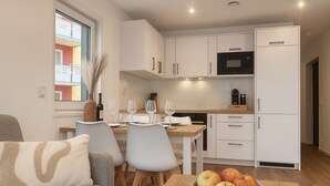 A modern kitchen with white cabinets, a microwave, and a refrigerator. There is a dining table with chairs and a vase with dried plants. - New Tiny House - cozy, private, family-friendly! (Hessisch Lichtenau)