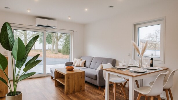 A modern living room with a grey sofa, wooden coffee table, and dining table set for four. - New Tiny House - cozy, private, family-friendly! (Hessisch Lichtenau)