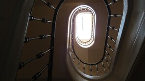 Un escalier en colimaçon, avec un luminaire central et une petite fenêtre en haut.