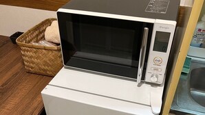 A compact microwave oven with a digital control panel, placed on a wooden table next to a wicker basket. - 30sec walk to Tsutenkaku/1 stop to Namba Sta./AH48 (Ebisu Higashi Naniwa-Ward,Osaka City)