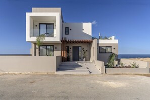 Una casa moderna de dos pisos amb un balcó, un vestíbul cobert i vistes al mar.
