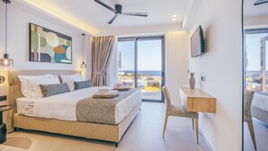 Quarto de hotel moderno com uma cama grande, uma escrivaninha, uma cadeira, um ventilador de teto e uma televisão.