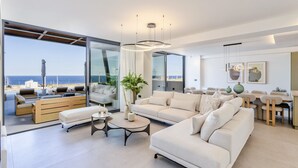 Sala de estar moderna com uma grande janela de vidro que dá para uma varanda com vista para o mar.