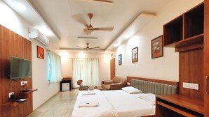 A hotel room with a large bed, a desk with a chair, a television, and a ceiling fan. - Hotel Meera Regency (Chiplun)