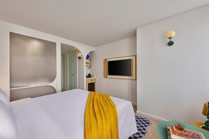 Une chambre d’hôtel avec un lit, une télévision, une petite table avec un verre et un tapis à carreaux.