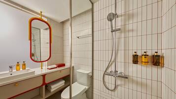 Une salle de bain moderne avec des toilettes blanches, un lavabo avec un miroir et une douche équipée d’un pommeau de douche à main.