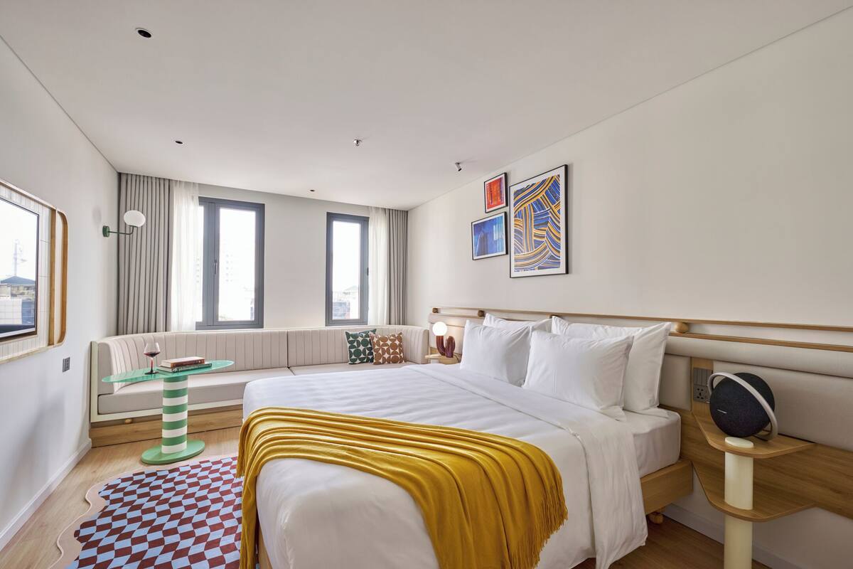Une chambre d’hôtel moderne avec un grand lit, un canapé, une petite table et des œuvres d’art accrochées aux murs.