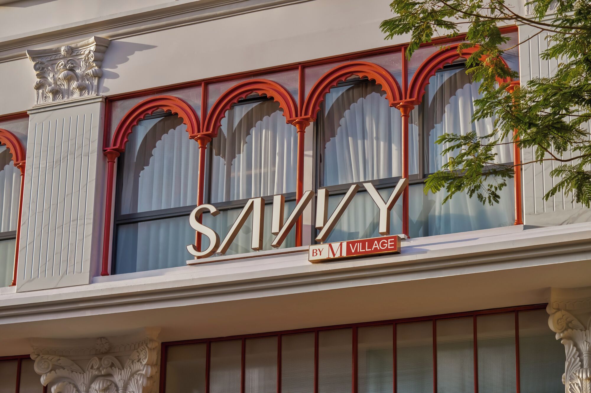 A building facade with large arched windows and a prominent sign that reads 'SAVINY BY M VILLAGE'.
