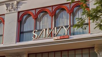A building facade with large arched windows and a prominent sign that reads 'SAVINY BY M VILLAGE'.