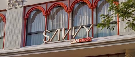 A building facade with large arched windows and a prominent sign that reads 'SAVINY BY M VILLAGE'.