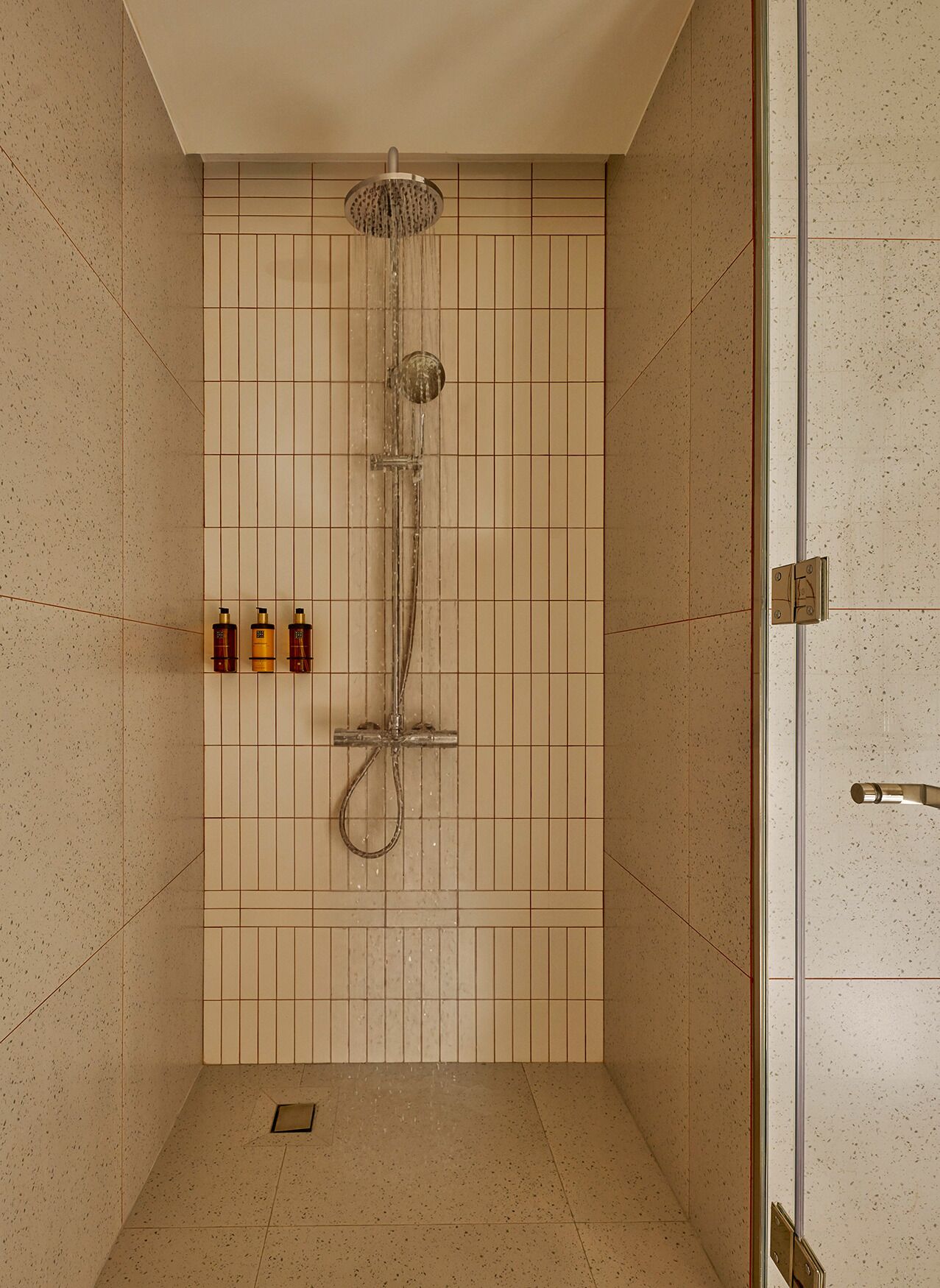 A shower with a handheld showerhead and a wall-mounted control panel.
