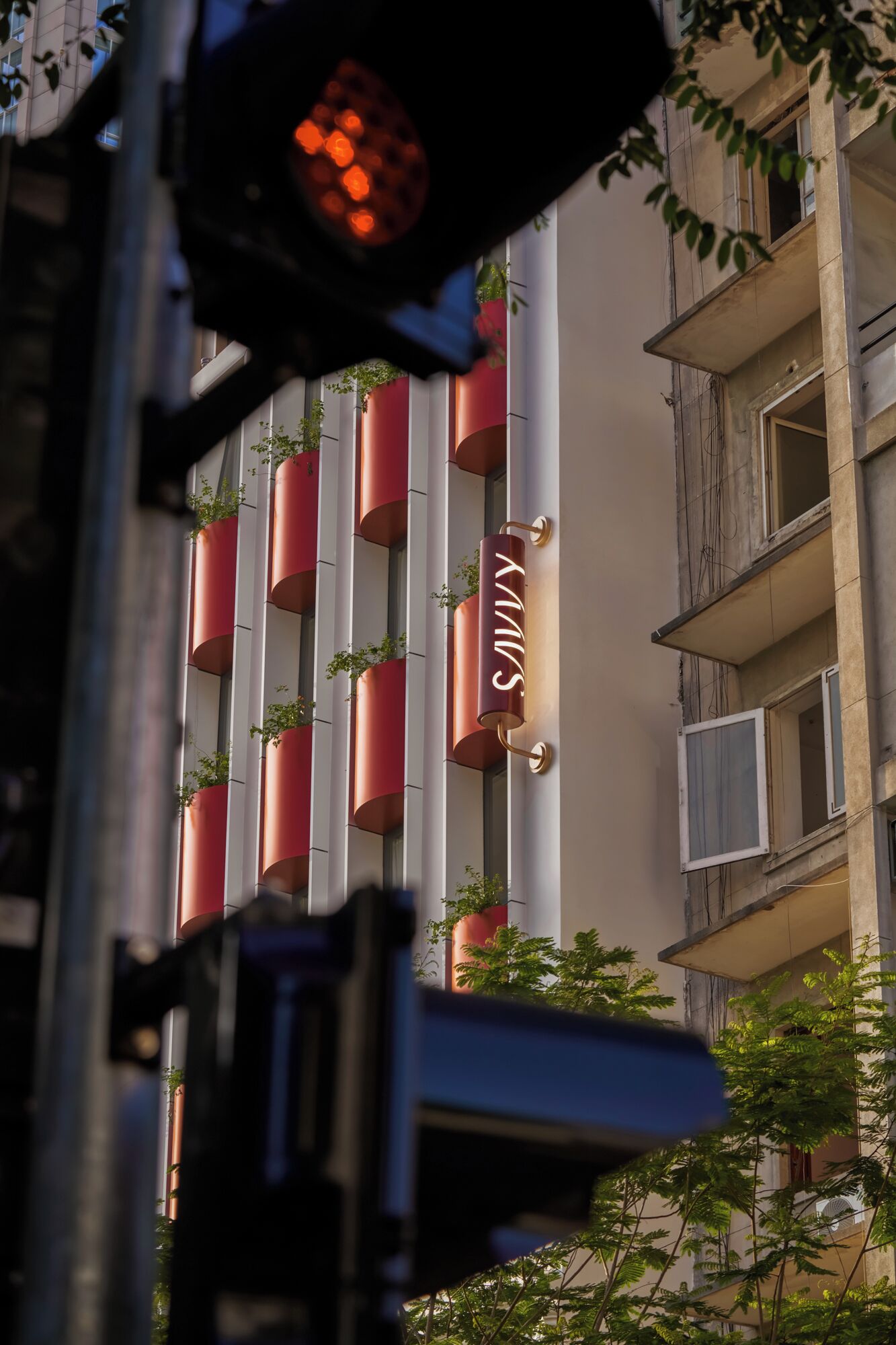 Un edificio con balcones verticales rojos, un letrero con las letras 'S' y 'M' visibles, y un semáforo al frente.