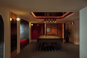 Une salle de billard avec une table de billard, un canapé rouge et une plante en pot.