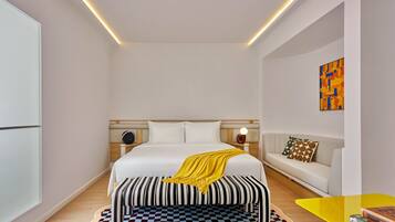 Un dormitorio moderno con una cama grande, mesitas de noche, un banco, un sofá y una pequeña mesa con libros.