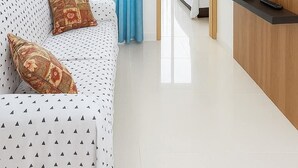 Et moderne hotelværelse med loftventilator, en sofa med mønstrede puder, et tv ophængt på væggen og udsigt til den udendørs balkon.