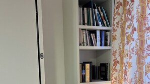 A bookshelf with books and a lamp, a grey sofa, and a floral curtain. - App. Red (Borgonovo)