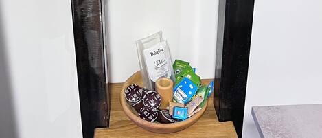 Una zona de cocina con una cafetera en un estante, un cuenco de vidrio y una bandeja con alimentos envasados.