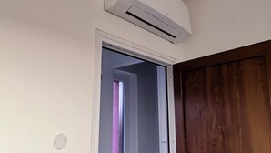 A room with a white wall, a wooden door, and an air conditioning unit mounted on the wall. - App. Red (Borgonovo)