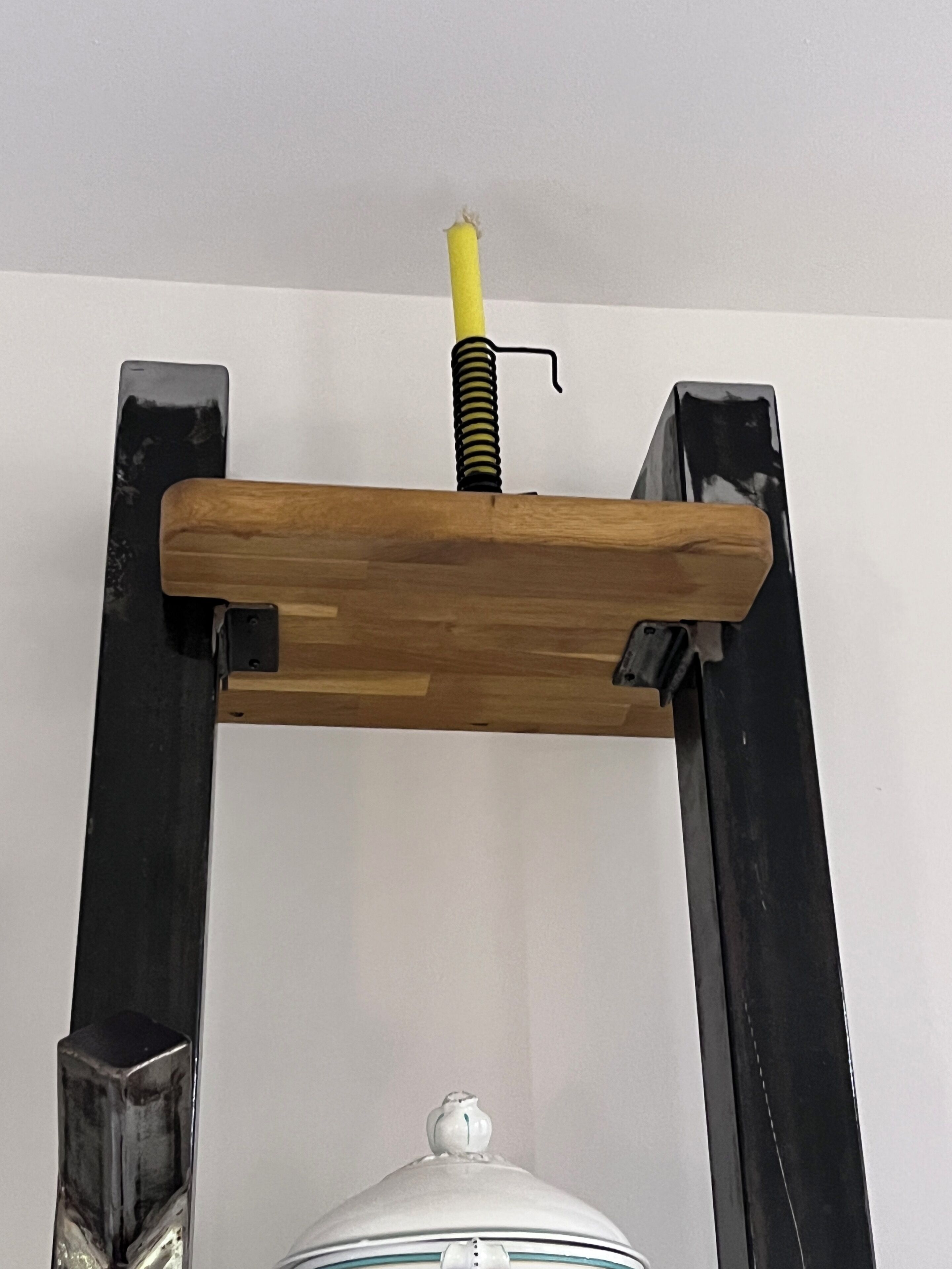 Une étagère en bois dotée d’un mécanisme à ressort jaune, fixée sur une structure en métal noir.