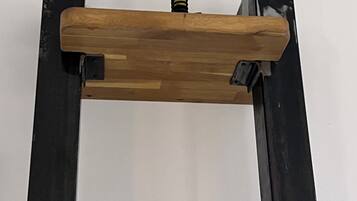 Une étagère en bois dotée d’un mécanisme à ressort jaune, fixée sur une structure en métal noir.