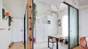 Et moderne interiør med trægulv, et spiseområde med bord og stole, en sofa og en skydedør, der fører ud til en balkon.