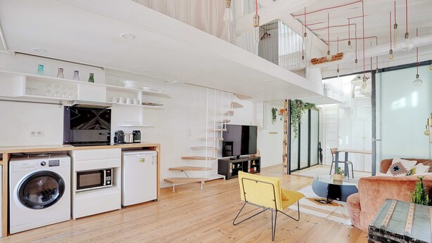 Et moderne køkken med indbyggede apparater, et spiseområde med sofa og bord, samt en trappe til et øvre plan.