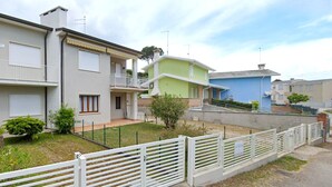 A residential area with houses, a white fence, and a grassy lawn. - Pleasant apartment in Rosolina Mare with balcony (Rosolina Mare (RO))