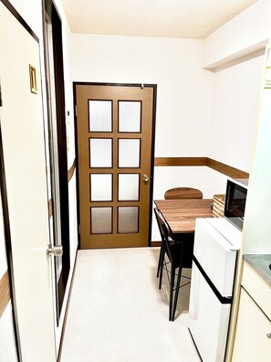 A small kitchen with a wooden door, a dining table, and a refrigerator. - 30sec walk to Tsutenkaku/1 stop to Namba Sta./AH55 (Ebisu Higashi Naniwa-Ward,Osaka City)